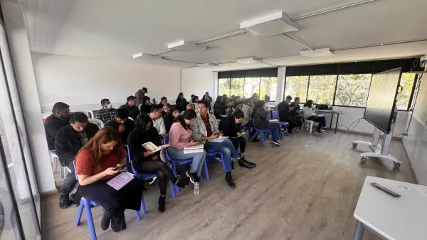 Estudiantes adultos en una sala de educación superior frente a una pantalla interactiva sobre ruedas