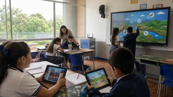 Dos estudiantes señalan un contenido en la pantalla interactiva mientras la docente acompaña a otros y dos más usan tableta y cuaderno