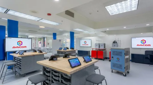 Aula STEAM con pantallas interactivas AVACOM, mesas de trabajo de madera con tabletas en soportes y un carro de carga de dispositivos